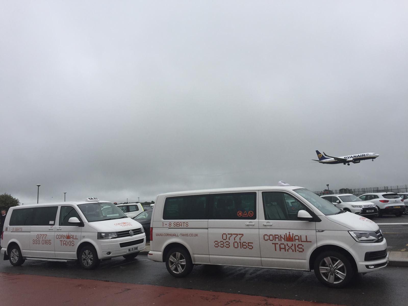Two Cornwall Taxis minibuses at the airport as a plane takes off