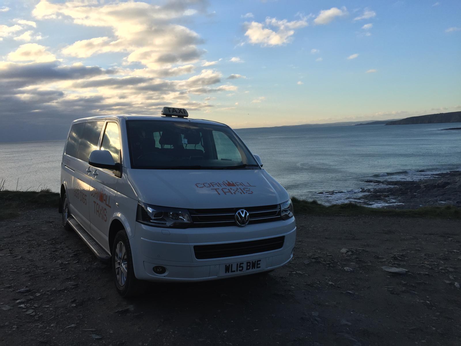 A Cornwall Taxis minibus beside the Cornish coast at sunset